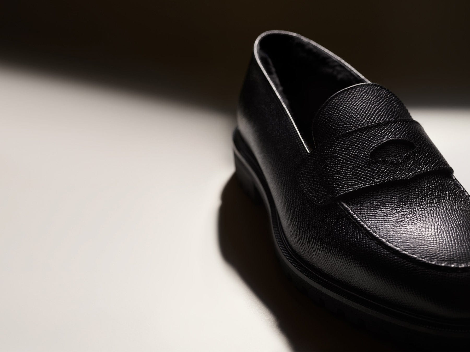 Black leather loafer shoe on a light surface with a dark background